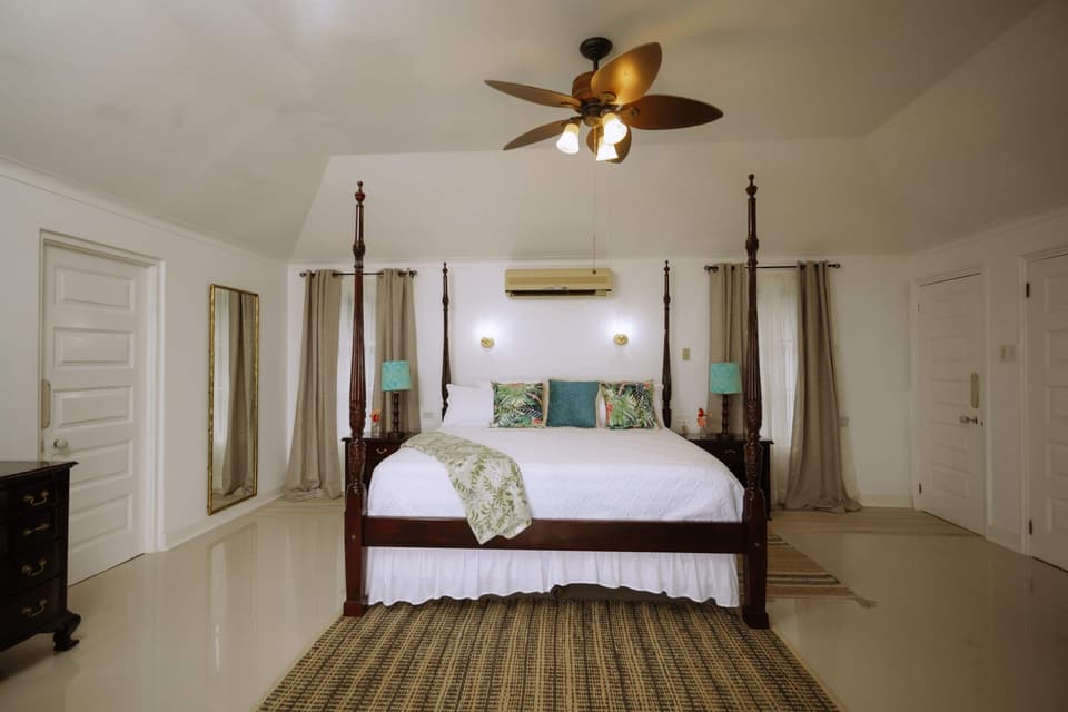 The four-poster king bed in the primary suite at Bay Vista Villa, with the balcony beyond